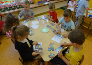 Sześcioro dzieci siedzi przy stoliku, każde dziecko układa historyjkę obrazkową.